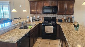 Una cocina moderna con encimeras de granito, un lavamanos de acero inoxidable, una estufa negra y un microondas.