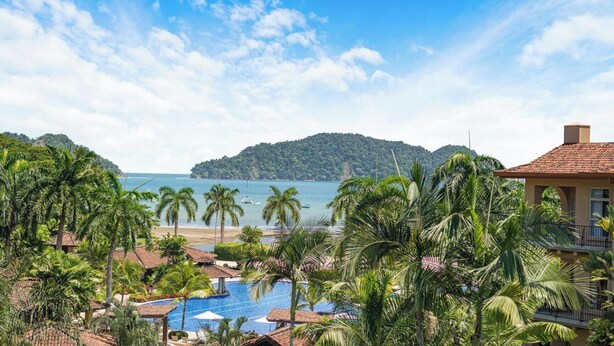 Un complexe hôtelier doté d’une piscine, de palmiers et offrant une vue sur la mer et une île lointaine.