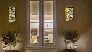 Une pièce avec une fenêtre, deux plantes en pot et des luminaires fixés au mur.