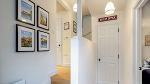 Un couloir orné de tableaux encadrés, un escalier et un panneau indiquant la zone des bureaux.