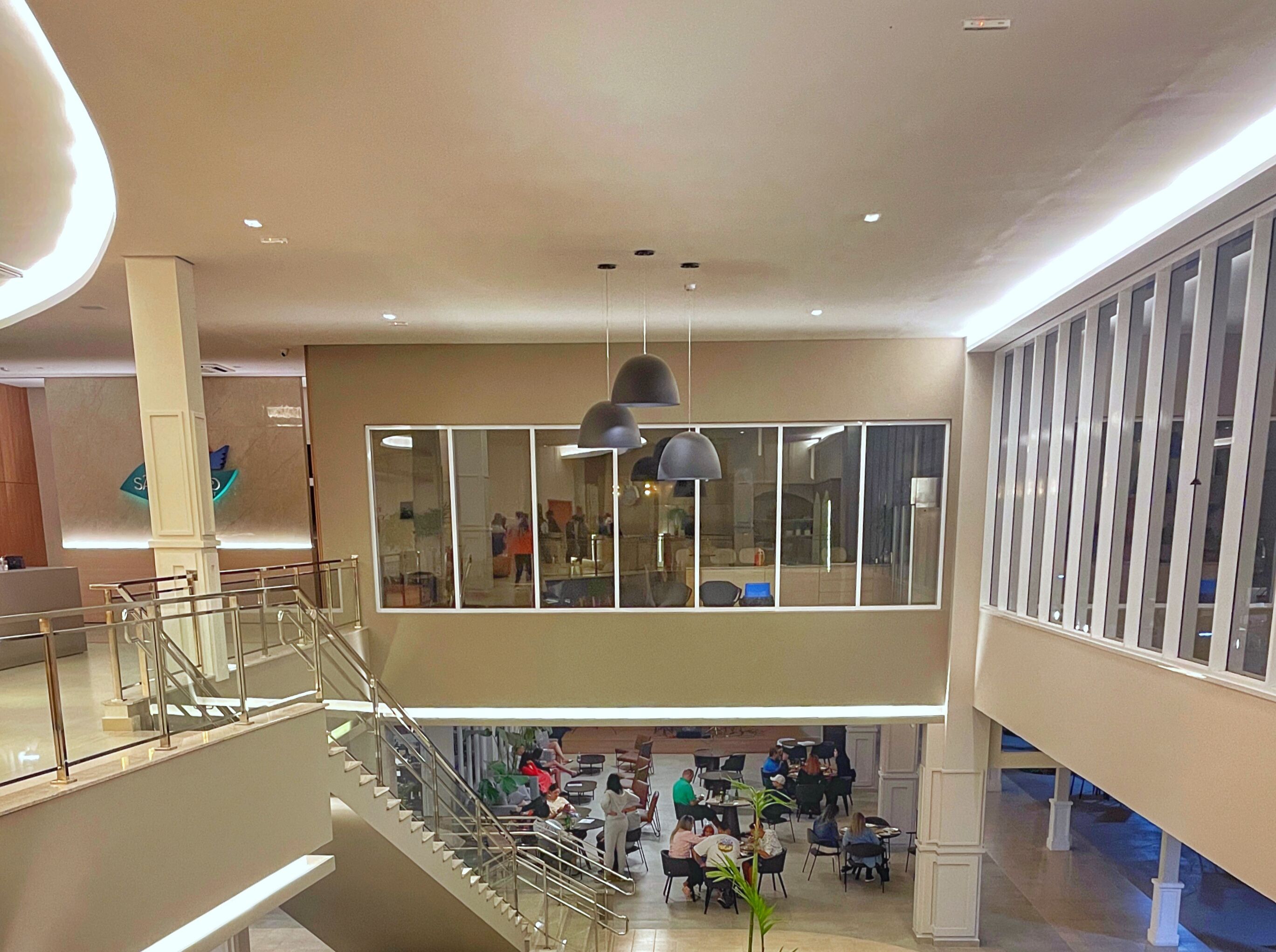 A spacious indoor area with a modern design, featuring a central staircase, multiple seating areas, and large windows allowing natural light.