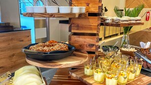 Una barra de buffet con diversos alimentos y bebidas, incluyendo un bol de frutas, una bandeja de pasteles y varios vasos de bebidas.