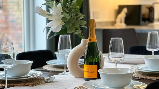 Ett matbord dukat med vita skålar, vinglas och en flaska champagne.