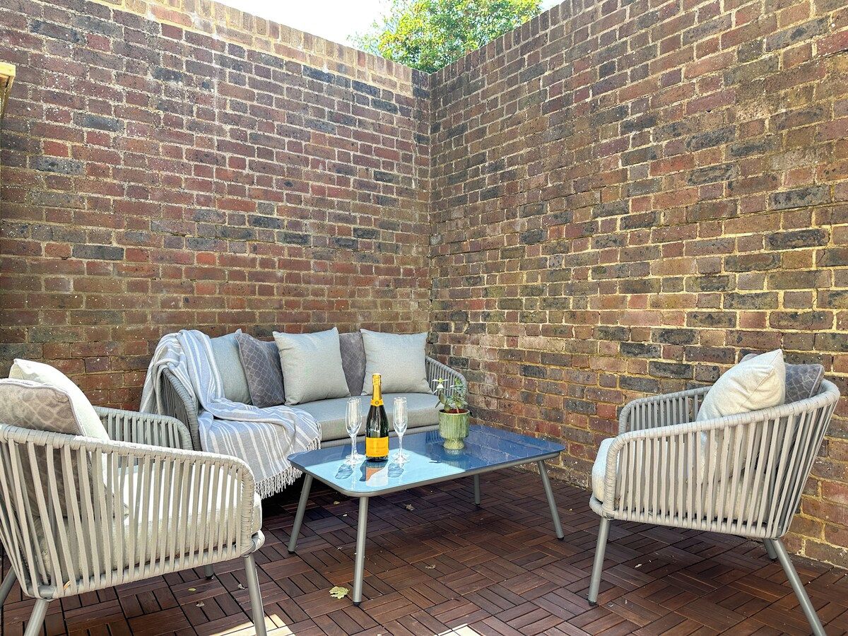 A patio area with a brick wall, wicker furniture, a glass table, and a bottle of champagne.