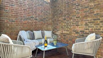 A patio area with a brick wall, wicker furniture, a glass table, and a bottle of champagne.