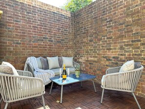 A patio area with a brick wall, wicker furniture, a glass table, and a bottle of champagne.
