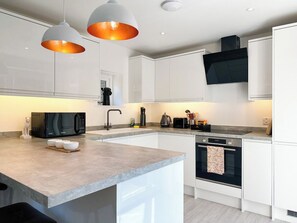 Una cocina moderna con armarios blancos, encimera de granito, microondas negro y horno empotrado.