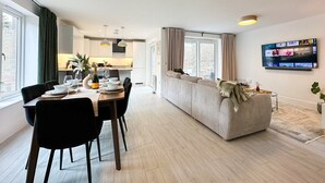 Ett modernt vardagsrum med en matplats, en soffa, en tv och ett kök i bakgrunden.