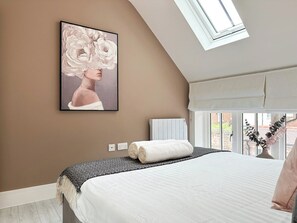 A bedroom with a bed, a skylight, a painting, and a window with a view.