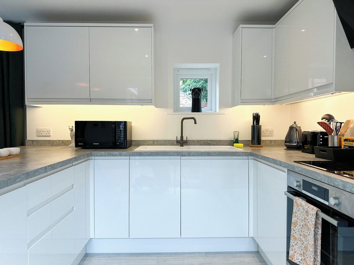 A modern kitchen with white cabinets, a black microwave, a sink, and a window above the sink.