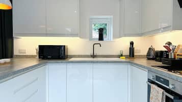 A modern kitchen with white cabinets, a black microwave, a sink, and a window above the sink.