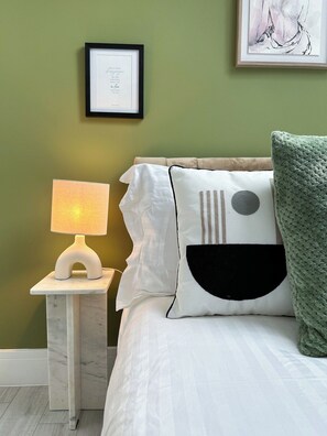 A bedroom with a bed, a nightstand with a lamp, a framed certificate on the wall, and a green throw blanket.