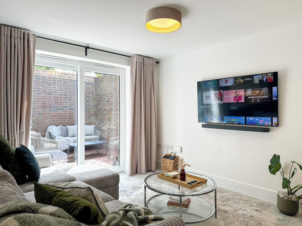 A living room with a sofa, a glass coffee table, a television mounted on the wall, and a sliding glass door leading to an outdoor area.