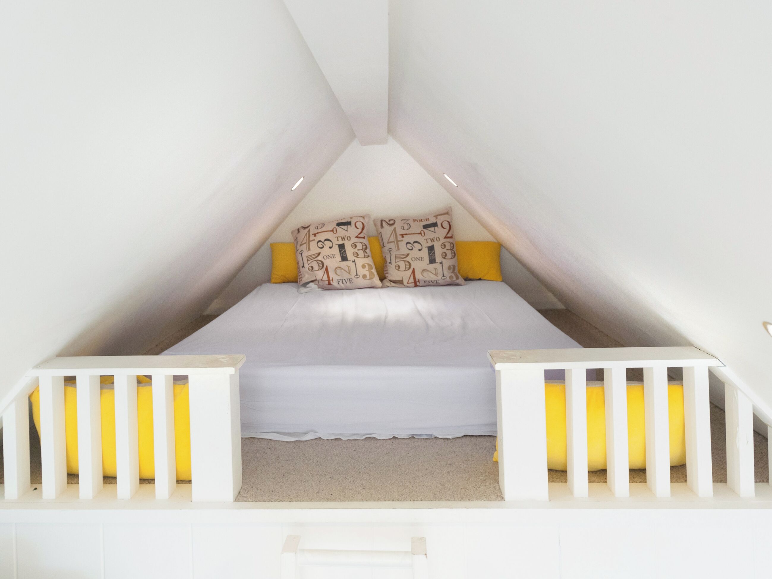 A triangular attic bedroom with a bed, pillows, and a white railing.