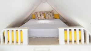 Ein quadratisches Schlafzimmer im Dachgeschoss mit Bett, Kissen und einer weißen Geländer.