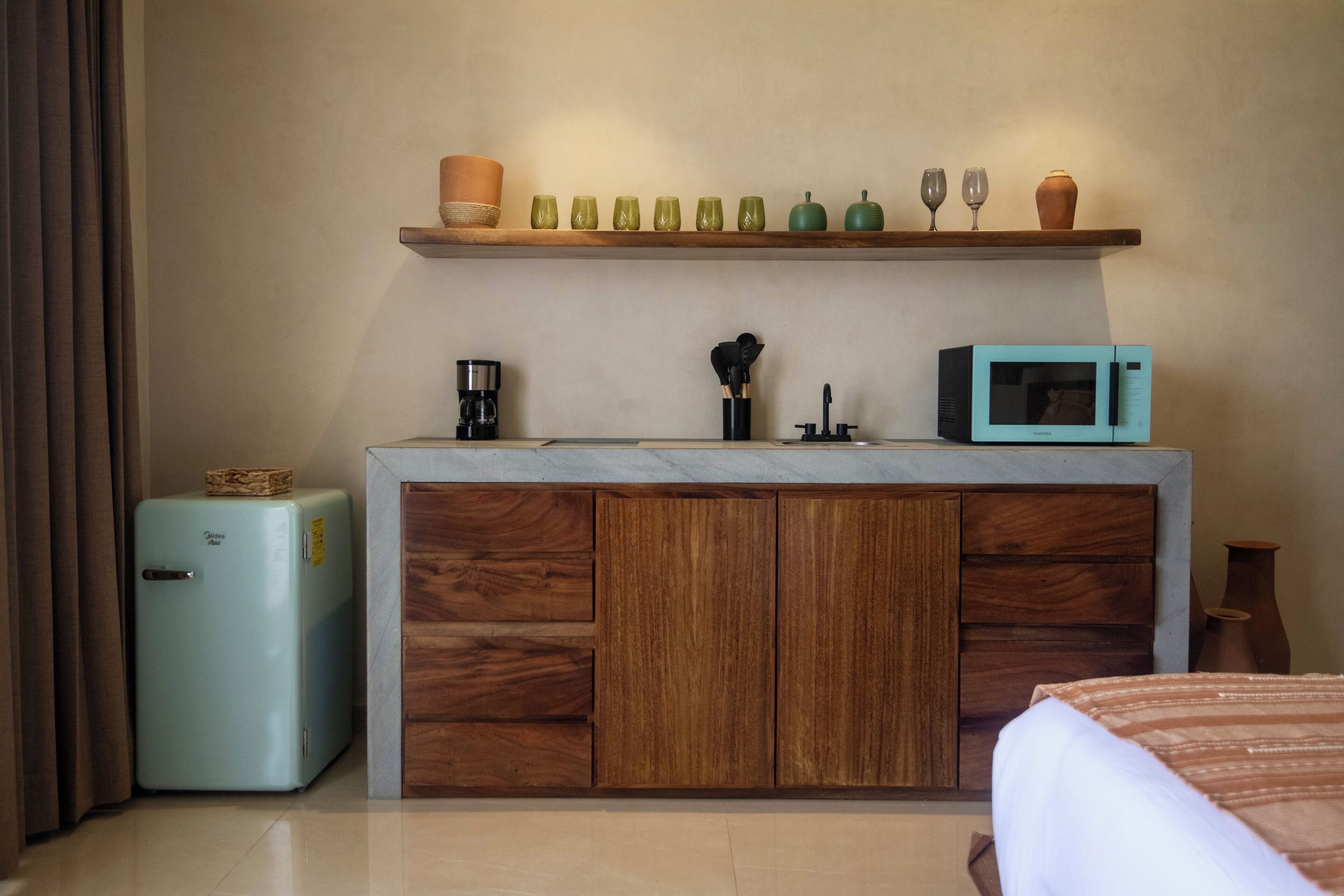 A compact kitchenette with a refrigerator, microwave, coffee maker, and wooden cabinets.