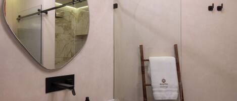 A bathroom with a wooden vanity, a large mirror, a towel rack, and a shower area.