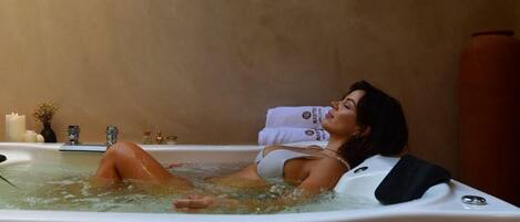 A person relaxing in a hot tub with a towel, surrounded by candles and a vase of flowers.
