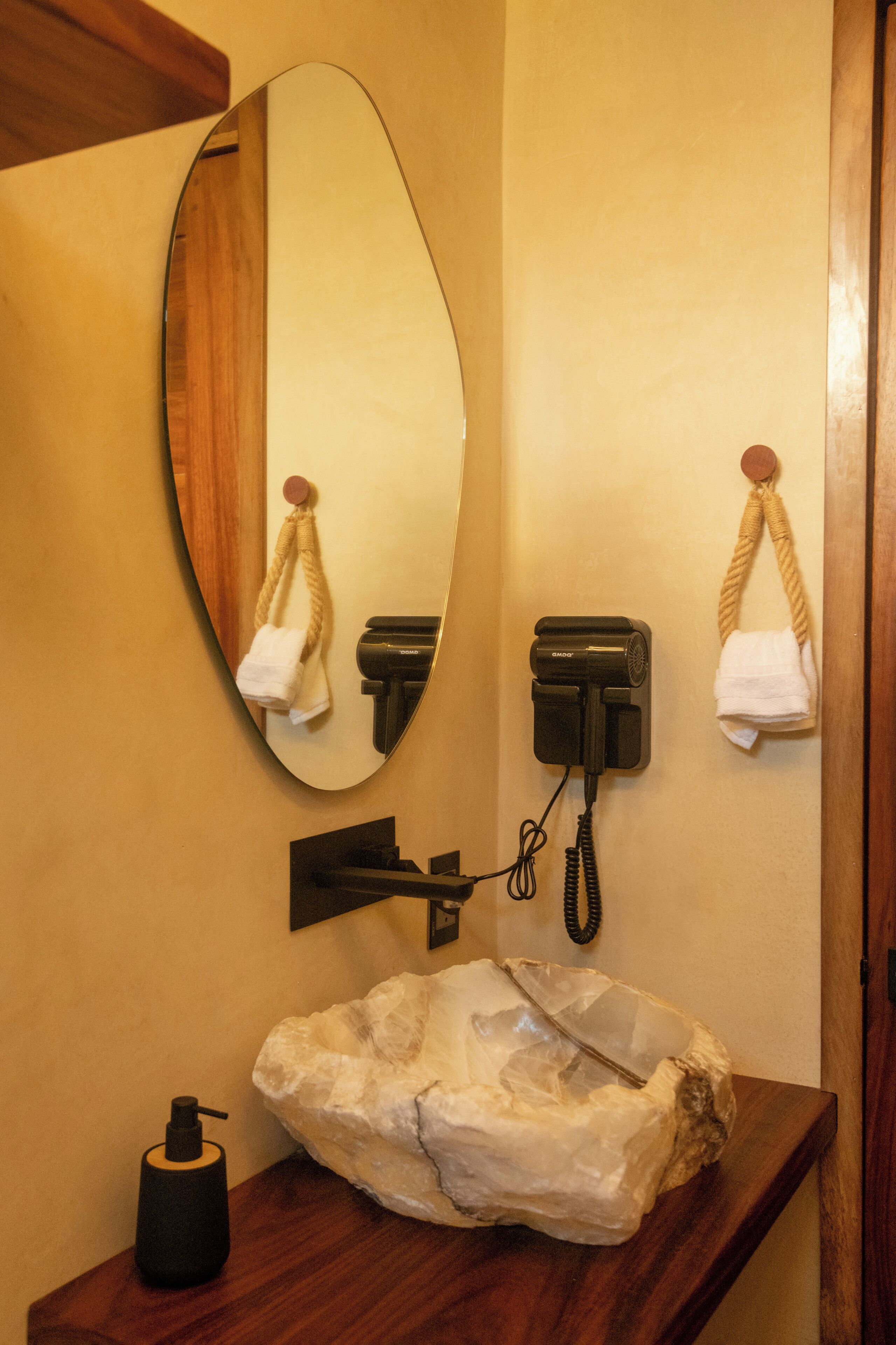 Un baño con tocador de madera, un espejo grande, un secador de pelo y dispensador de jabón.