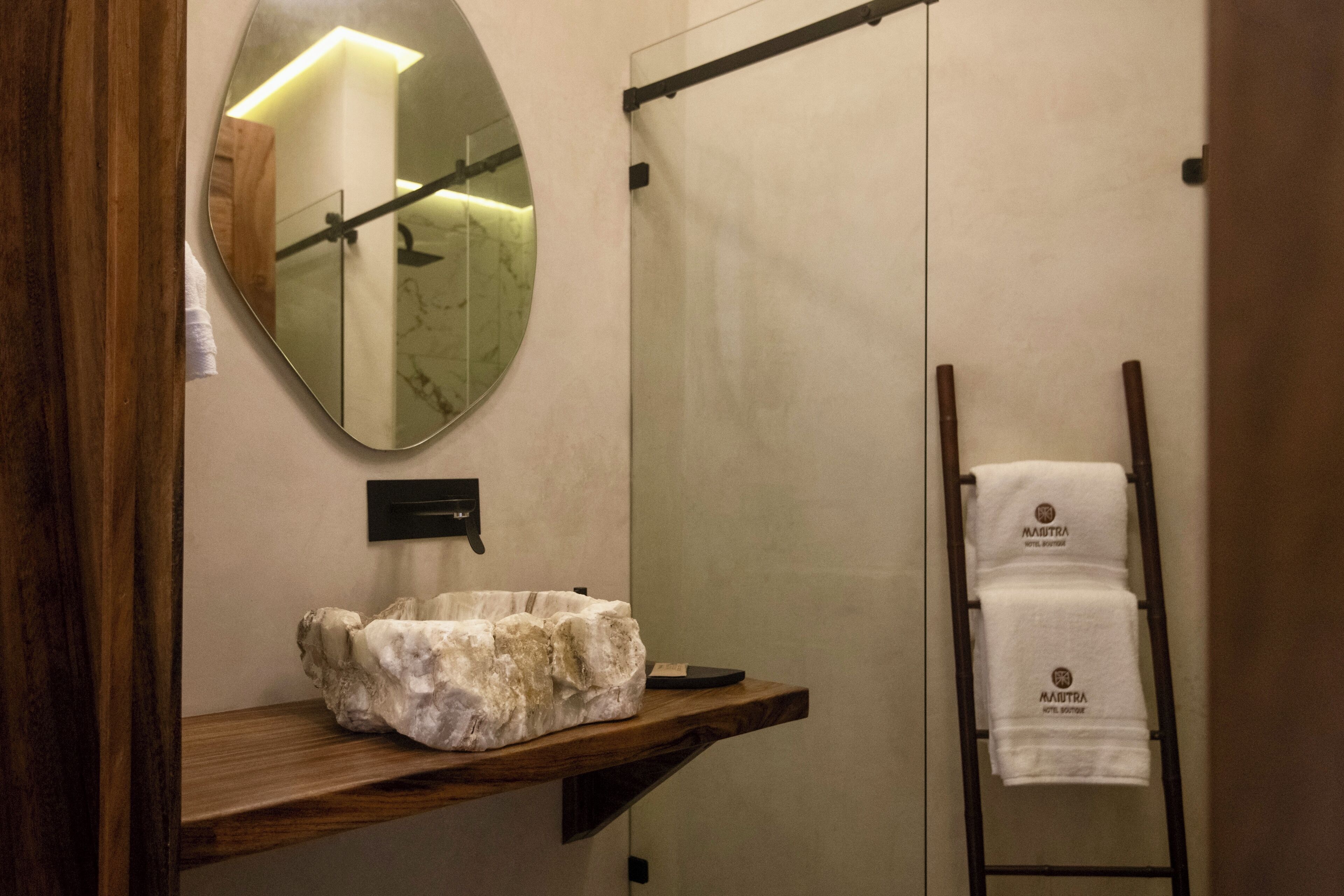 Un baño con lavamanos de mármol, estante de madera, toallero y espejo.