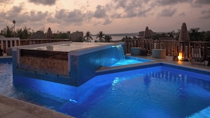 A swimming pool with a waterfall feature, surrounded by lounge chairs and a view of the ocean at sunset. - Mantra Hotel Boutique (Brisas de Zicatela)