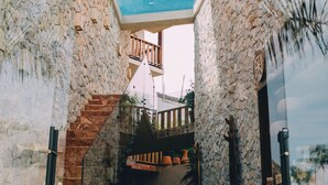 A stone-walled interior with a staircase leading to a balcony, potted plants, and a hanging light fixture. - Mantra Hotel Boutique (Brisas de Zicatela)