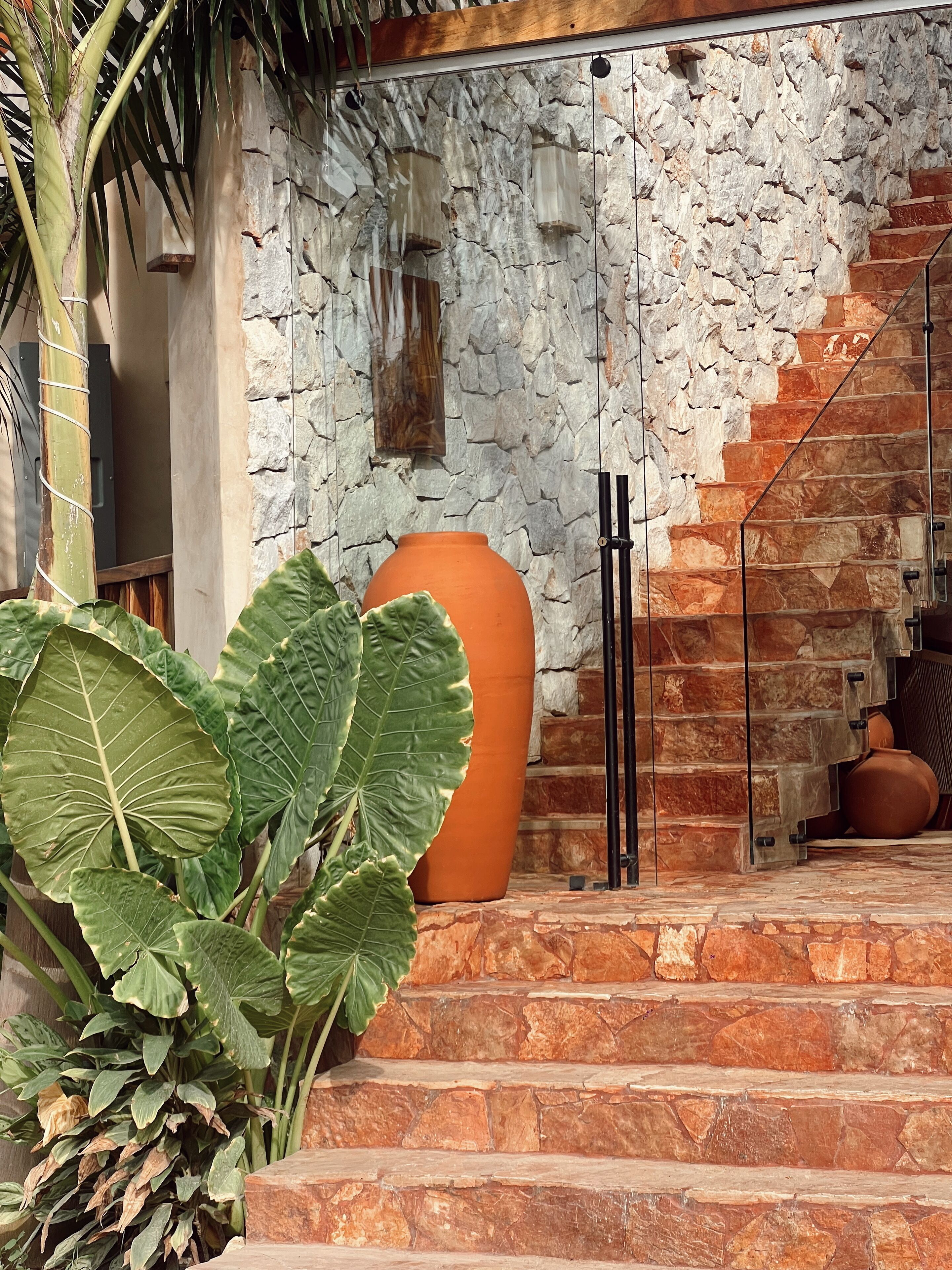 A staircase leading to a room with a stone wall and a large terracotta pot.