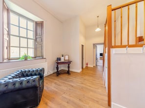Une pièce spacieuse avec un plancher en bois, un canapé en cuir noir, une table en bois ornée d’une plante et un tableau blanc.