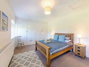 Un dormitorio con cama de madera, mesitas de noche, una silla, un armario y una alfombra estampada.