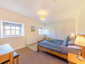 Une chambre à coucher comprenant un lit, une table de chevet, une lampe, une fenêtre avec des stores, un radiateur et un tableau accroché au mur.