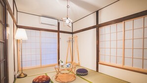 Une pièce de style japonais traditionnel, avec un sol recouvert de tatamis, des paravents shoji, un luminaire suspendu en forme d’étoile, une petite table avec un plateau en verre et une lampe sur pied.