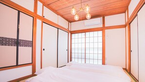 Une chambre de style japonais traditionnel, avec un sol recouvert de tatamis, un grand lit, des portes coulissantes et un plafond en bois.