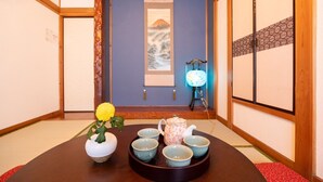 Une pièce de style japonais traditionnel, avec un sol recouvert de tatamis, une porte coulissante en papier de riz (shoji), une petite table sur laquelle est disposé un service à thé, et une lampe décorative.