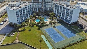Un hotel de varios pisos con piscina, canchas de tenis y vistas al océano.