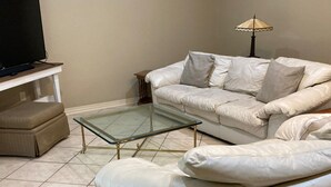 A living room with a white sofa, a glass coffee table, a television on a stand, and a floor lamp. - BestStays@King Bee. Large Groups OK.TVs in rooms
 (Tyler)