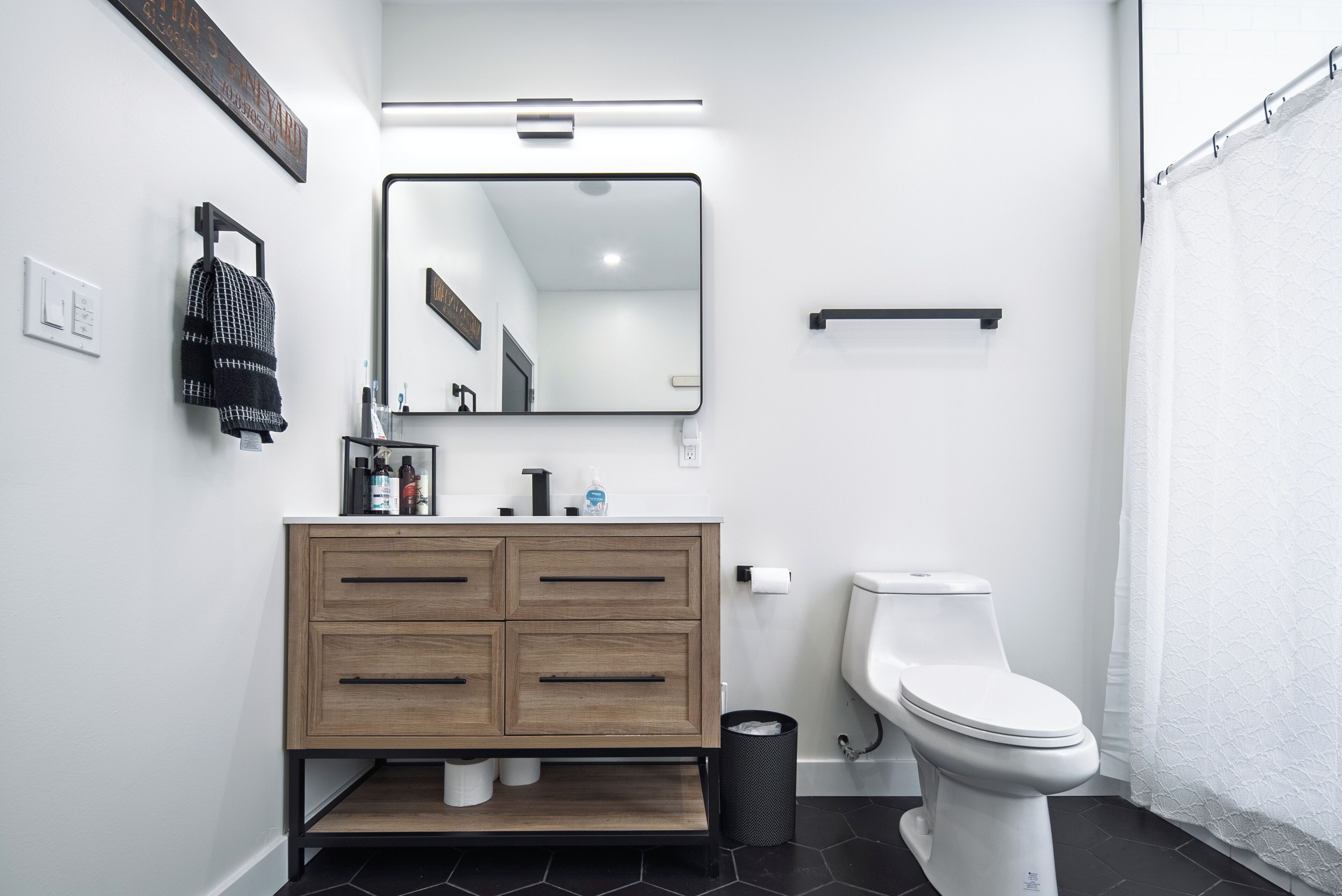 A modern bathroom with a wooden vanity, a white toilet, and a shower curtain.