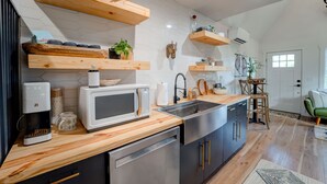 Una cocina moderna con estantes de madera, microondas, pileta y lavavajillas.