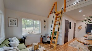 Una sala de estar acogedora con un sofá verde, una escalera de madera y un ventanal con vistas al exterior.