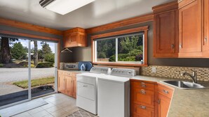 A compact kitchen with wooden cabinets, a built-in washer and dryer, a large window, and a sink. - Rainier Ranch & Poolside Escape (Enumclaw)