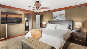 A bedroom with a large bed, a bench, a ceiling fan, a nightstand, and a painting of a landscape. - Rainier Ranch & Poolside Escape (Enumclaw)