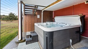 Un jacuzzi en un área exterior cubierta con vista a un campo verde y un edificio rojo al fondo.