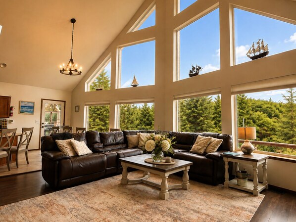 A spacious living room with a large sectional sofa, a coffee table, and a view of a forest through large windows.