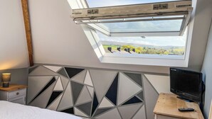 A bedroom with a skylight, a bed, a TV, and a bedside table.