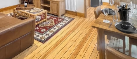 A cozy living room with a wooden floor, a TV on a wooden stand, a sofa, a coffee table, and a dining area with a table and chairs.