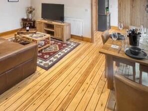 A cozy living room with a wooden floor, a TV on a wooden stand, a sofa, a coffee table, and a dining area with a table and chairs.