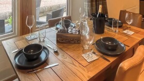 Une table à manger dressée avec des assiettes noires, des couverts et des verres à vin, ainsi qu’une bouteille de champagne et un pichet posés sur la table.