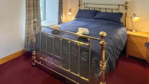 Un lit bien fait, avec un cadre en métal, un matelas bleu et un oreiller blanc. Une table de chevet avec une lampe s’y trouve.