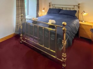 A neatly made bed with a metal frame, a blue mattress, and a white pillow. There is a bedside table with a lamp on it. - Stewards Bothy - UK48303 (Berwick-upon-Tweed)
