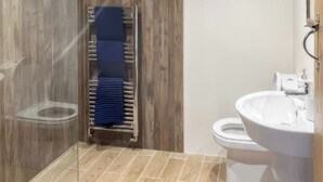 Une salle de bain avec un plancher en bois, une douche en verre, un lavabo blanc et un porte-serviettes avec une serviette bleue.