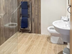 A bathroom with a wooden floor, a glass shower enclosure, a white sink, and a towel rack with a blue towel. - Stewards Bothy - UK48303 (Berwick-upon-Tweed)